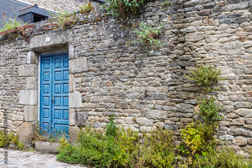 Ancient wall with large nature bricks overgrown by wild flowers with blue weathered doorin Dinan in Cotes-d'Armor, Brittany, France