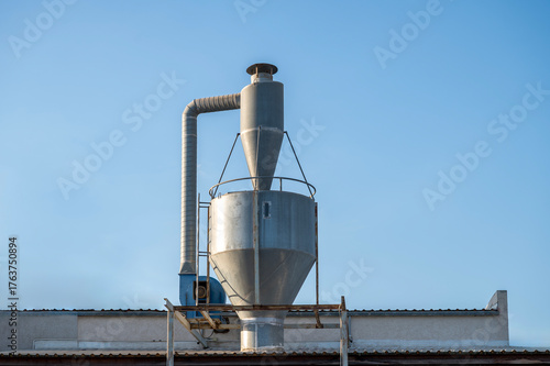 Industrial metal chimney and ventilation system on factory rooftop under clear blue sky.