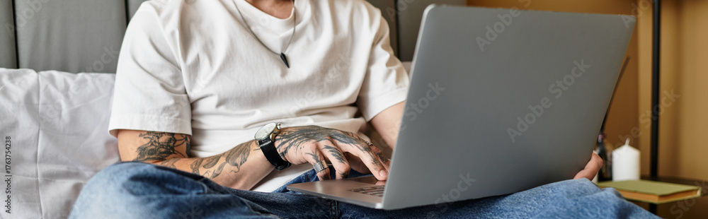 Fototapeta premium Young man in stylish apartment focused on laptop while sitting comfortably on bed