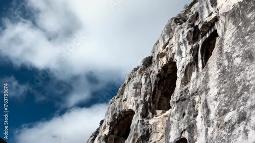Dramatic Mountain Cliff Face With Natural Caves Underneath a Cloudy Blue Sky In Daylight