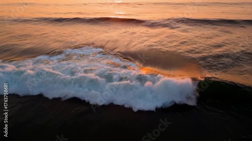 Dramatic Ocean Wave Crashing During Golden Hour Sunset with Warm Sunlight Reflecting on Rippling Water