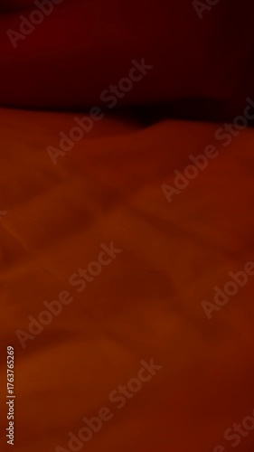 Vertical video. Fingers Pressing Snooze Button on Smartphone Alarm Set for 6 AM on Bed in Dim Orange Light Morning Sleepiness