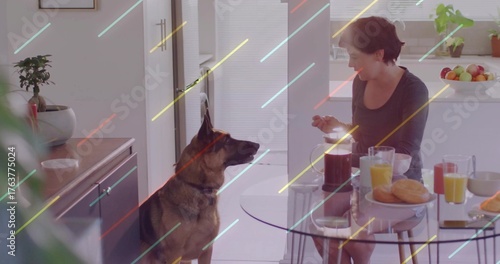 Sitting mid-adult woman sipping orange juice at glass table in kitchen, with German shepherd