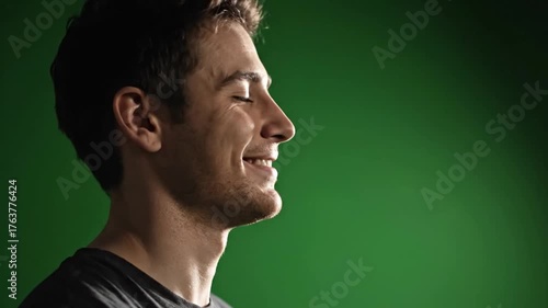 Profile of a Young Man with Short Brown Hair and Light Skin, Looking Down Thoughtfully Against a Solid Green Background, Capture of Serene Emotional Expression in Studio Portrait Photography for