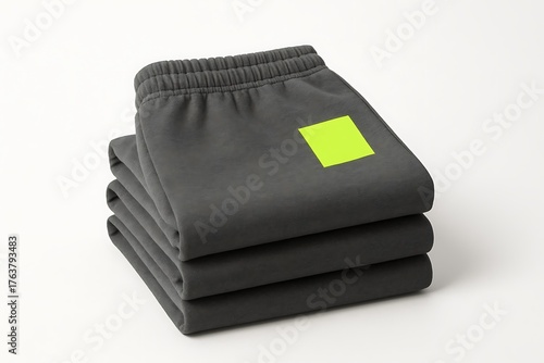 Stack of folded dark gray sweatpants with bright green square logo