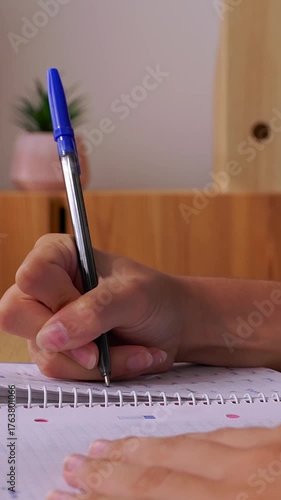 Vertical HD video of young student girl writing notes in her notebook while studying at home, with a laptop and textbooks nearby