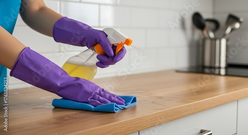Person in purple gloves cleaning a wooden kitchen counter with spray and cloth.