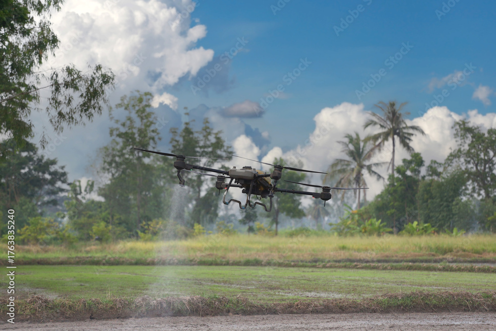 Fototapeta premium A drone effectively sprays pesticide over a farm field surrounded by lush green trees.