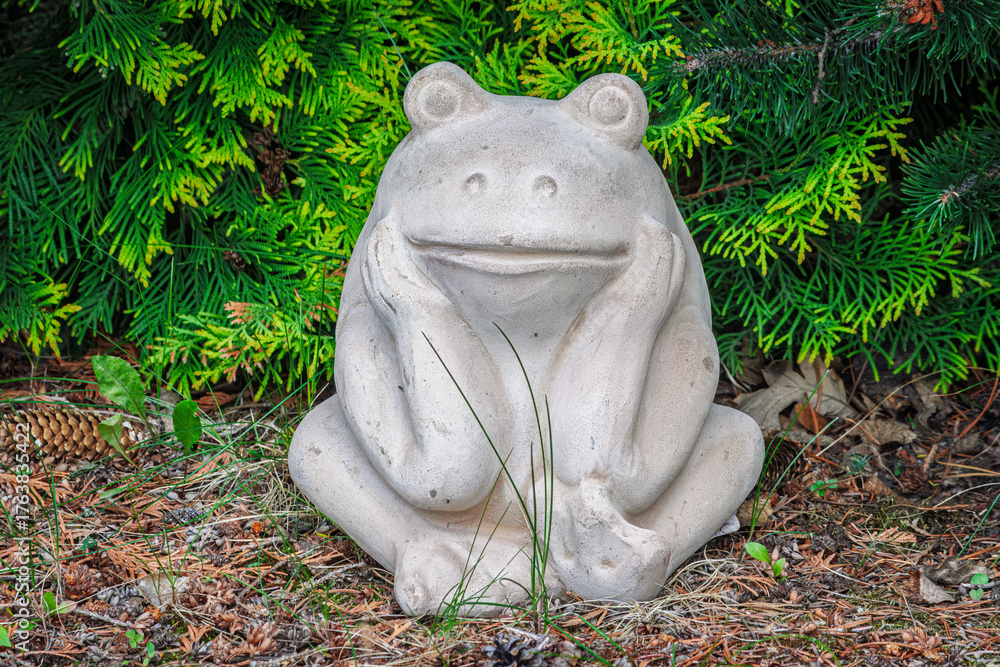 Obraz premium Garden statue of a frog in a thinking pose with green foliage and grass