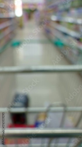 Vertical video. First-Person View Through an Empty Shopping Cart Moving Down a Bright Supermarket Aisle, Colorful Shelves Out of Focus, Consumerism Concept