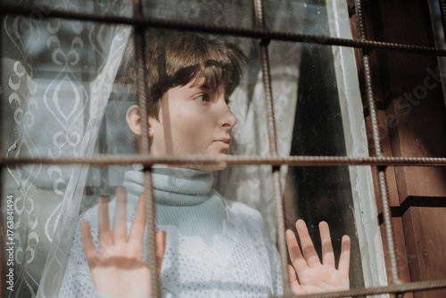 Tableau sur toile Poor sad orphan girl looking out of window.