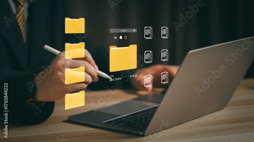 Photos Businessman using digital file management system on laptop, organizing folders and documents in virtual interface