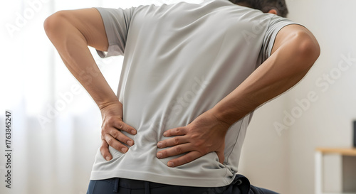 Man experiencing sharp lower back pain clutching his aching spine in discomfort and seeking relief, a common ailment affecting millions daily.