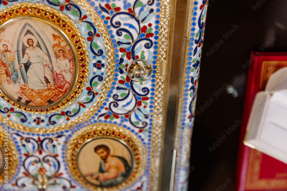 Obraz premium A close-up detail of a traditional Orthodox Christian Gospel book, richly decorated with gold, colorful enamel patterns, and religious icons of Jesus and saints