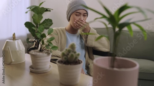 Young Asian woman with cancer is sitting alone in a wheelchair and coughing after chemotherapy with recovery and relieve her symptoms in the living room at her home. Domestic lifestyle after illness. 