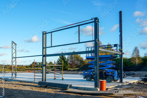 Steel frame structure and scissor lift at construction site under clear blue sky