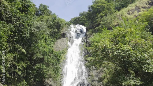 Majestic Waterfall Cascading Down Lush Green Cliff Amidst Clear Sky and Vibrant Nature Surroundings