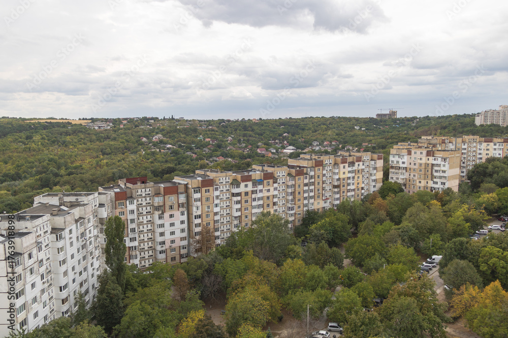 Fototapeta premium Panoramic city view showing residential apartment buildings and green forest hills under cloudy autumn sky in Chisinau,