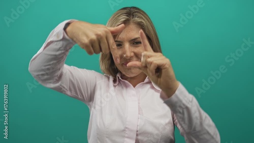 Woman confidently framing view with her precise focused hands in a teal studio setting; creativity perspective.