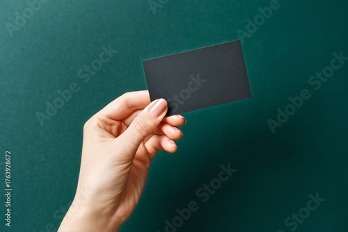 Hand Holding a Blank Card Against a Dark Green Background With Stylishly Desi...