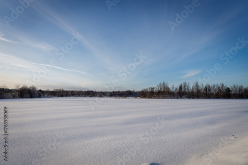 Vast snow-covered field under a serene blue sky with wispy clouds and distant forest — tranquil, minimalist winter landscape perfect for peace, nature, or seasonal themes.