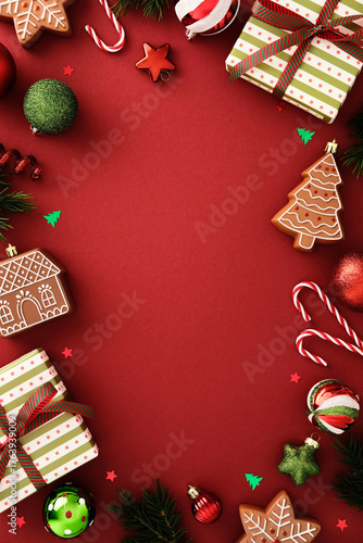 Christmas border flat lay with gifts, gingerbread cookies, candy canes and baubles on red background. Festive holiday frame with copy space for seasonal design © photoguns