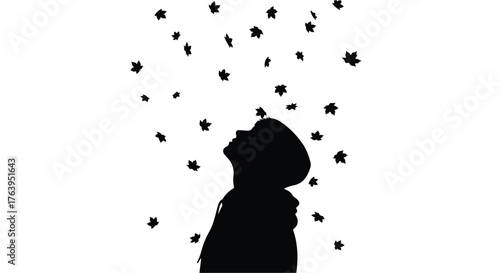 Child in silhouette looking up at falling leaves