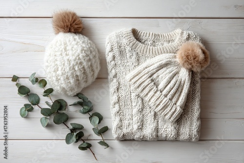 Cozy White Sweater and Hat Set Arranged on a Wooden Surface With Greenery Acc...