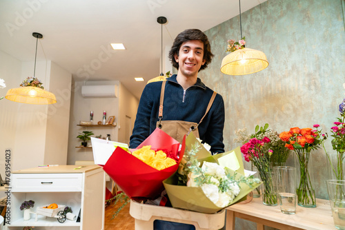 Fotografie Young florist smiling holding fresh flower bouquets in shop