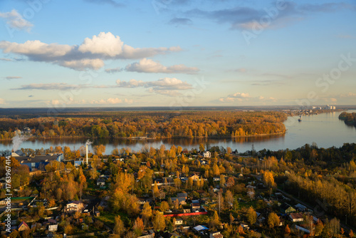 A picturesque scene unfolds with vibrant autumn foliage surrounding a tranquil river. Boats glide across the reflective water as the sun sets, casting warm hues across the sky