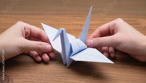 Skillful Hands Shape Blue Paper Into a Beautiful Origami Crane on a Wooden Table