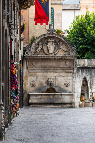 View of an ornate stone fountain with intricate carvings stands proudly beneath a vibrant banner in the historic square, Sulmona, Abruzzo, Italy.