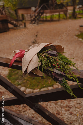 A Christmas bouquet is lying on a wooden fence. The bouquet is decorated in craft and red rent. Interior bouquet of coniferous branches. Vertical photo.