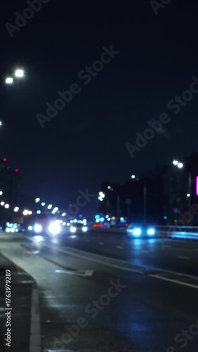 Night city road with glowing headlights and reflections on wet asphalt, modern urban traffic and moody blue light atmosphere
