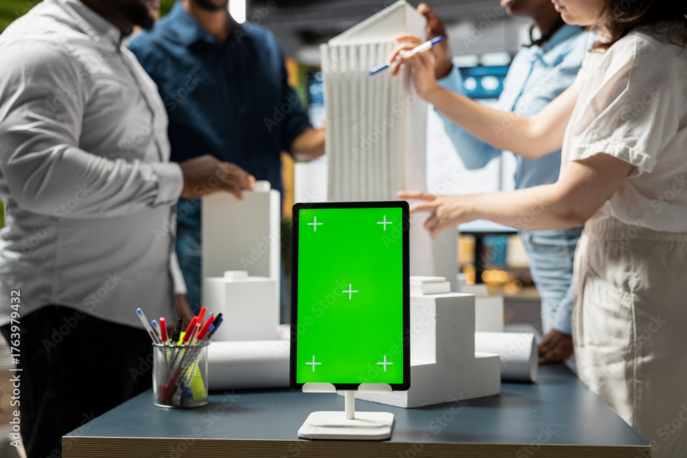 Obraz premium Engineers team share master plan ideas next to chroma key display, using 3D architectural models and blueprints for construction layout details. Modern design city planning in a session.