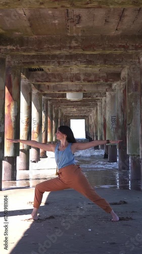 Woman practicing yoga warrior pose under a sunny wooden pier structure