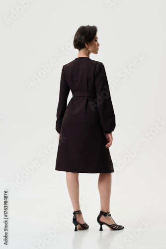 A pregnant model girl in stylish clothes poses on a white background.