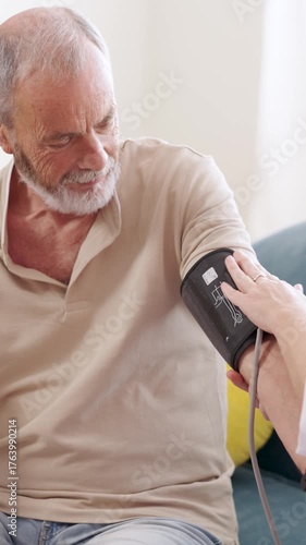 Nurse checking elderly man blood pressure at home. Vertical