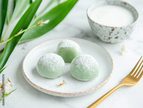 Soft, pastel-green Pandan Mochi, lightly dusted with rice flour, rest on a minimalist white ceramic plate. A small golden fork lies beside the plate.