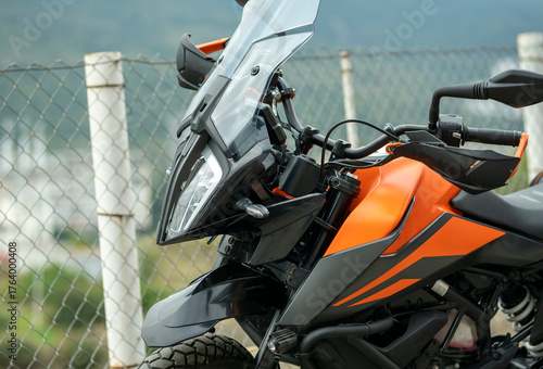 A view of a black and orange recreational motorcycle with saddlebags. Its various components and mechanisms are visible. A view of the front end during the day.