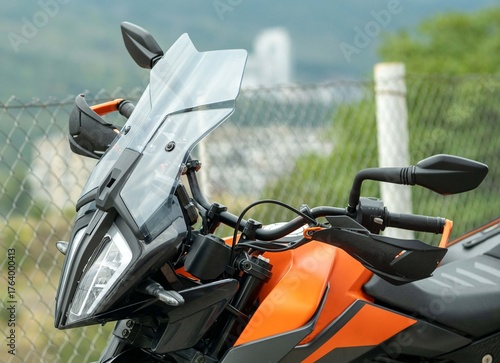 A view of a black and orange recreational motorcycle with saddlebags. Its various components and mechanisms are visible. A view of the front end during the day.