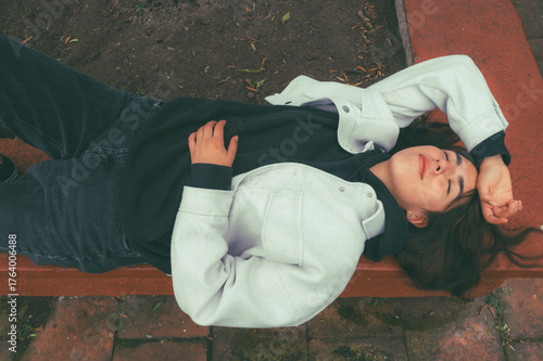 Young Latina girl wearing fall clothes lying on a planter, very relaxed taking a nap
