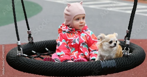 A one-year-old girl sits on a swing in a park