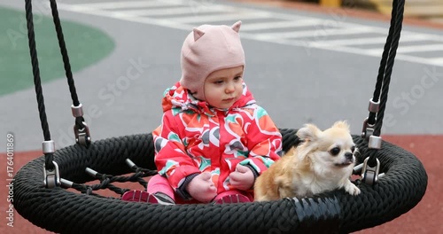A one-year-old girl sits on a swing in a park