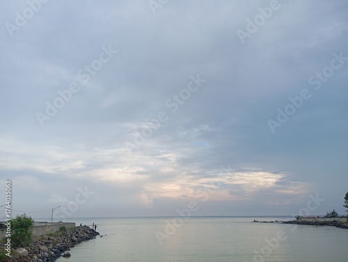 A calm seascape under a cloudy sky during twilight, showing gentle waves meeting rocky shores and a peaceful horizon with soft pastel hues reflecting on the water