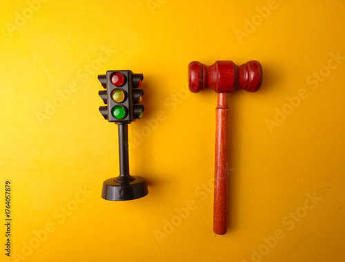 The image shows a miniature traffic light and a gavel on a yellow background