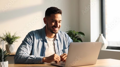 Young Man Smiling While Working on Laptop in Modern Office Space