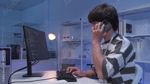 Young male Asian IT freelancer programmer and tech engineer remotely works with computer and mobile phone, software codes for application development, and web network system information data in room.