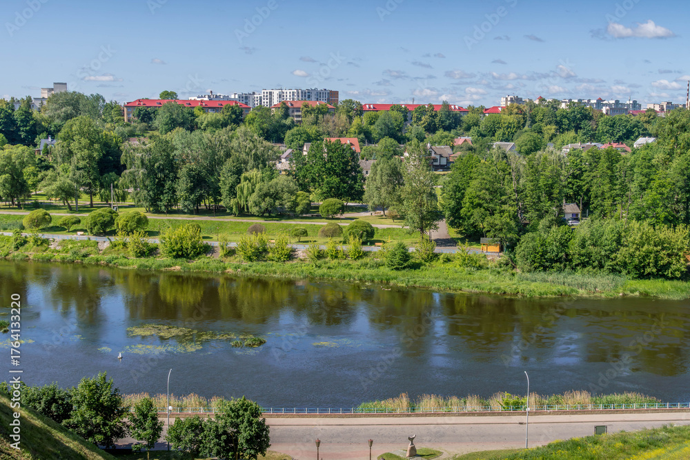 Fototapeta premium Neman River flowing through green hills in Hrodna, Belarus above the lush riverside landscape. 