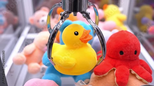 Bright yellow rubber duck toy captured by a claw machine in a game arcade.